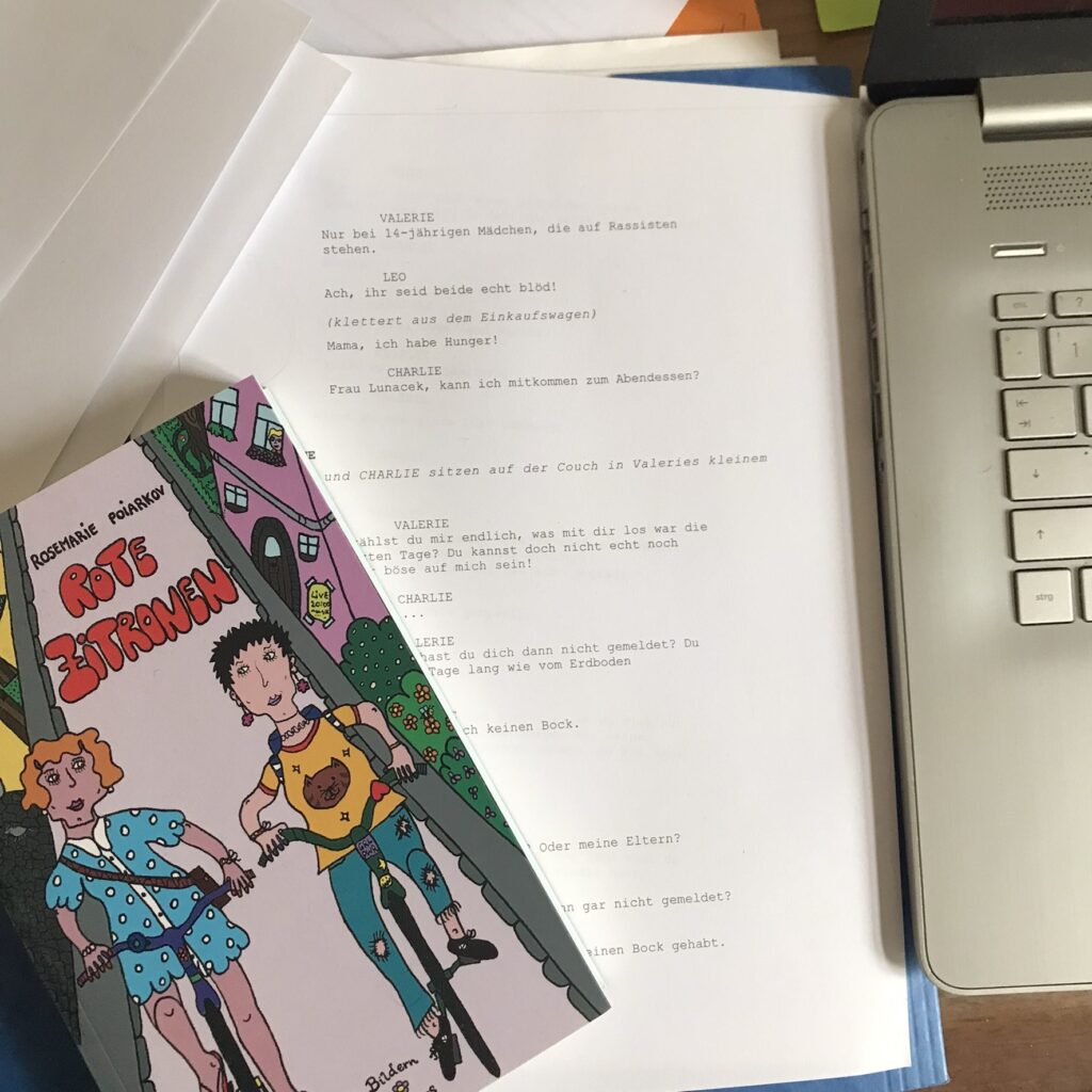 Buch "Rote Zitronen" auf einer Manuskriptseite, rechts ist ein kleiner Teil der Tastatur eines Laptops zu sehen